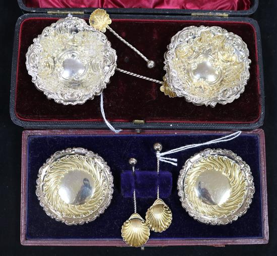 A pair of embossed silver-gilt salts with shell spoons and a similar set of fluted salts, both cased